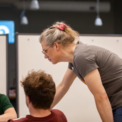Erin Cornelius站在一个学生的肩膀上看着笔记本电脑. 右边是另一个红头发穿绿色t恤的学生