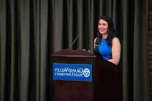 Woman in blue stands at a podium with 'Grand valley State University' logo on it