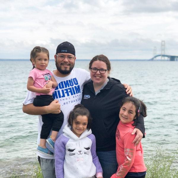 一家人的照片，带着三个小女儿，在湖岸附近，背景是麦基诺大桥