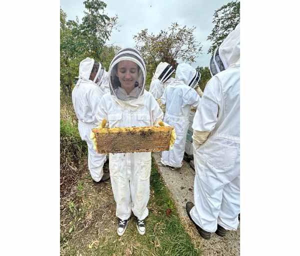 people in white beekeeper suits, one person in front holding a hive