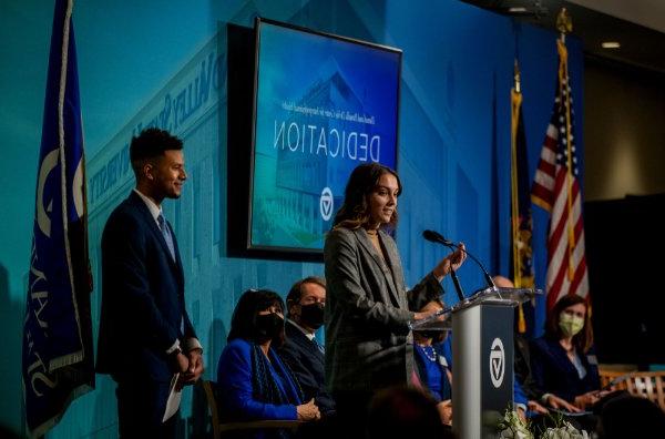 内科助理研究项目的学生Zoie Hulst在讲台上发言. Nursing student Jared Gordon stands beside her.