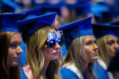 一位毕业生坐在毕业典礼上，眼睛上方戴着一副写着“2023届毕业生”的太阳镜. 