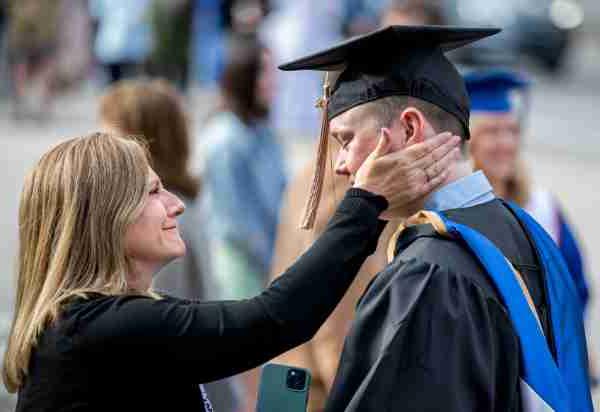 毕业典礼后，一位毕业生向他的母亲致意，母亲将一只手放在他的脸颊上.