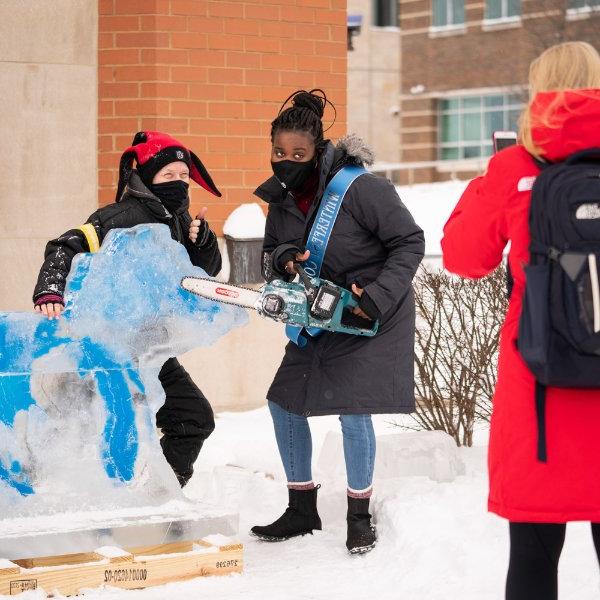 在GVSU冬季活动期间，一名学生与密歇根州和五大湖的冰雕合影.