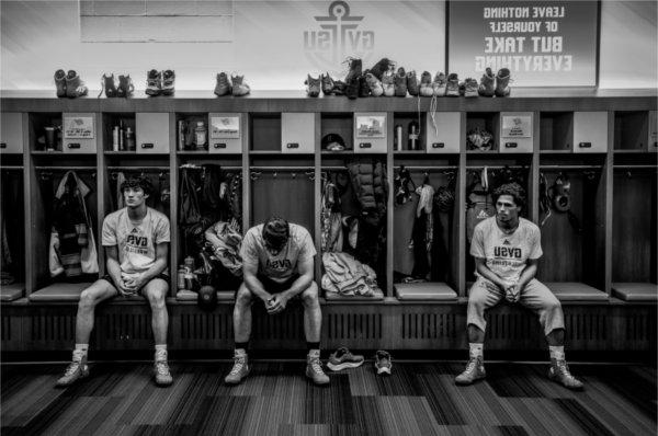 Three male wrestlers sit on the bench in the wrestling locker rooms in anticipation of the upcoming event.