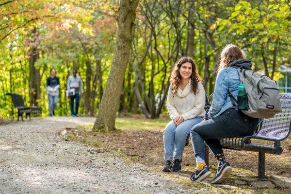 大学生们微笑着坐在树林里的长椅上，其他学生在后面走着.  