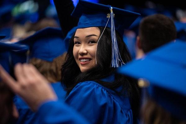  毕业典礼上，一名大学生头戴蓝色帽子，身穿蓝色长袍，从身后望过去.