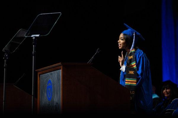  一位戴着毕业典礼帽、身穿毕业礼服的大学生在讲台上演讲. 