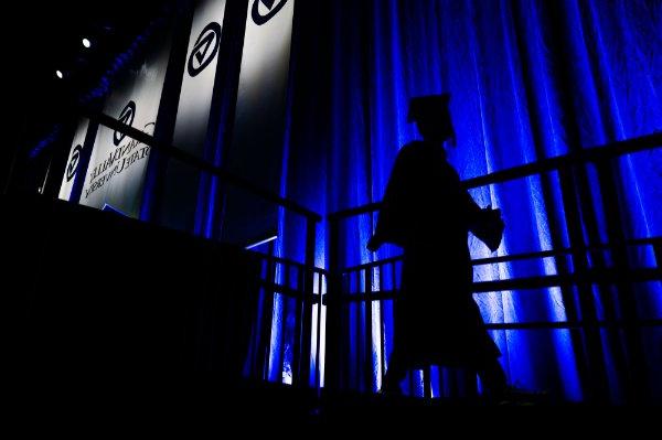  毕业典礼上，一名大学生离开舞台时，在蓝色幕布的映衬下露出了剪影. 