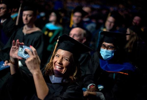 毕业典礼上，一名学生走过讲台，一名大学教员在拍照时大笑.  