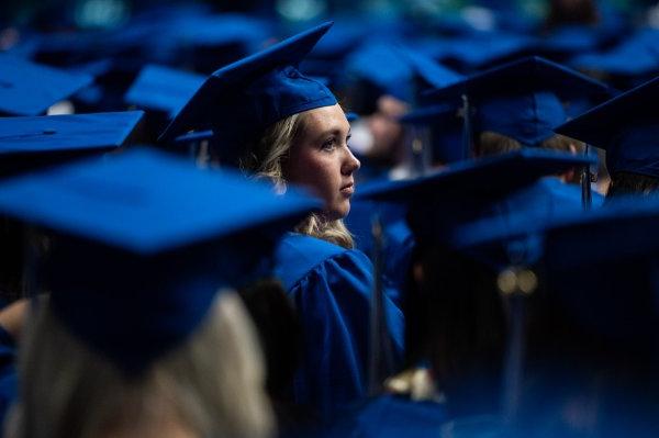  毕业典礼上，一名戴着蓝色帽子、身穿蓝色长袍的大学生被其他毕业生围在一起. 
