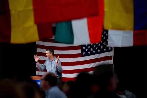 尼古拉斯Maodush-Pitzer, 布兰福德小学六年级老师, stands at podium with arms raised; American flag in background, 天花板上悬挂的其他旗帜