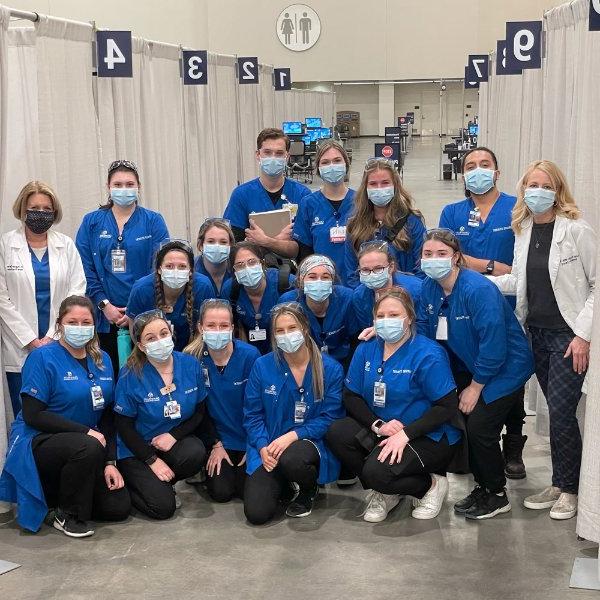 柯克霍夫护理学院的教员, 穿着白大褂, 还有穿蓝色擦洗衫的学生, 在大急流城疫苗诊所的照片.