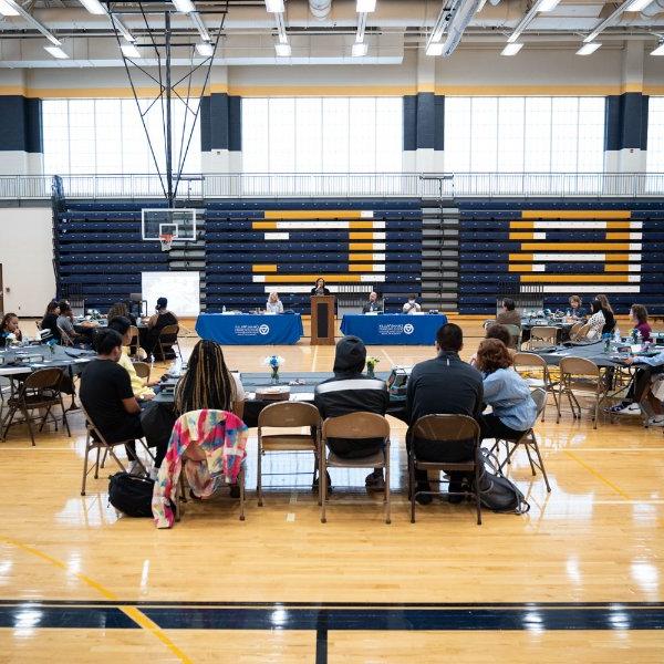 tables in a gymnasium with people seated around them; head table has blue drapes with GVSU logo. 背景中的露天看台是蓝色的，上面有大大的金色的B和C