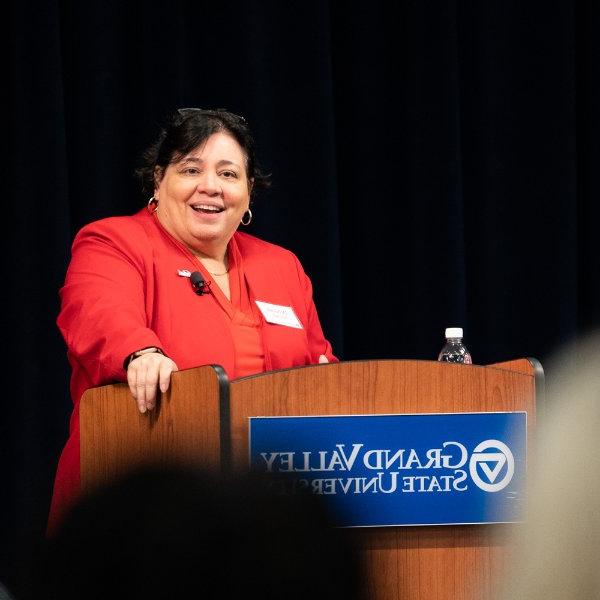 卓越教育(Excelencia in Education)联合创始人兼首席执行官Deborah Santiago站在讲台上发言. 她穿着一件红色的夹克.