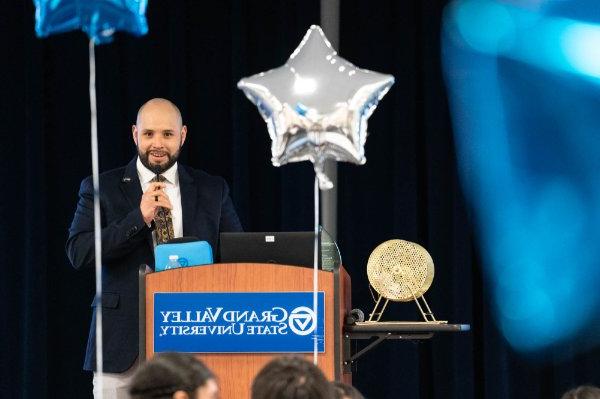 朱利安·拉米雷斯-托雷斯在讲台上对着麦克风讲话, 2个气球架在讲台上, 前景中的另一个蓝色气球