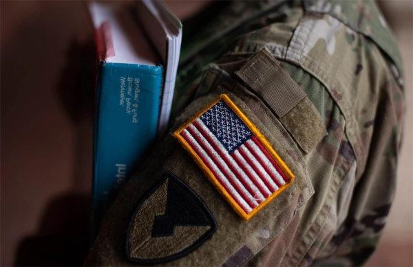 穿着印有美国国旗的军装的人的手臂上拿着书.