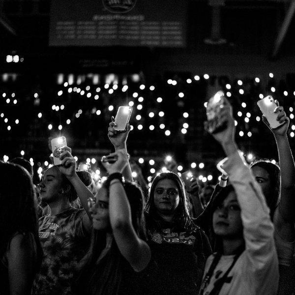 学生们在舞台上举起他们的手机来发光. 到处都可以看到灯光.