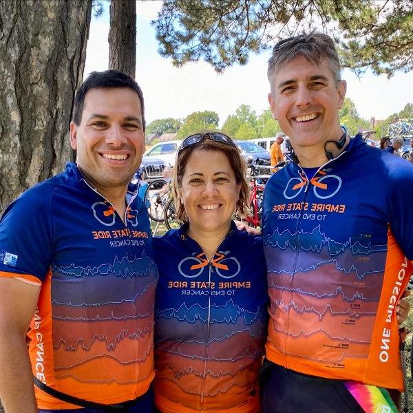 三人站在自行车衬衫上，用亮蓝色和橙色标明帝国之旅, 站在一棵树前
